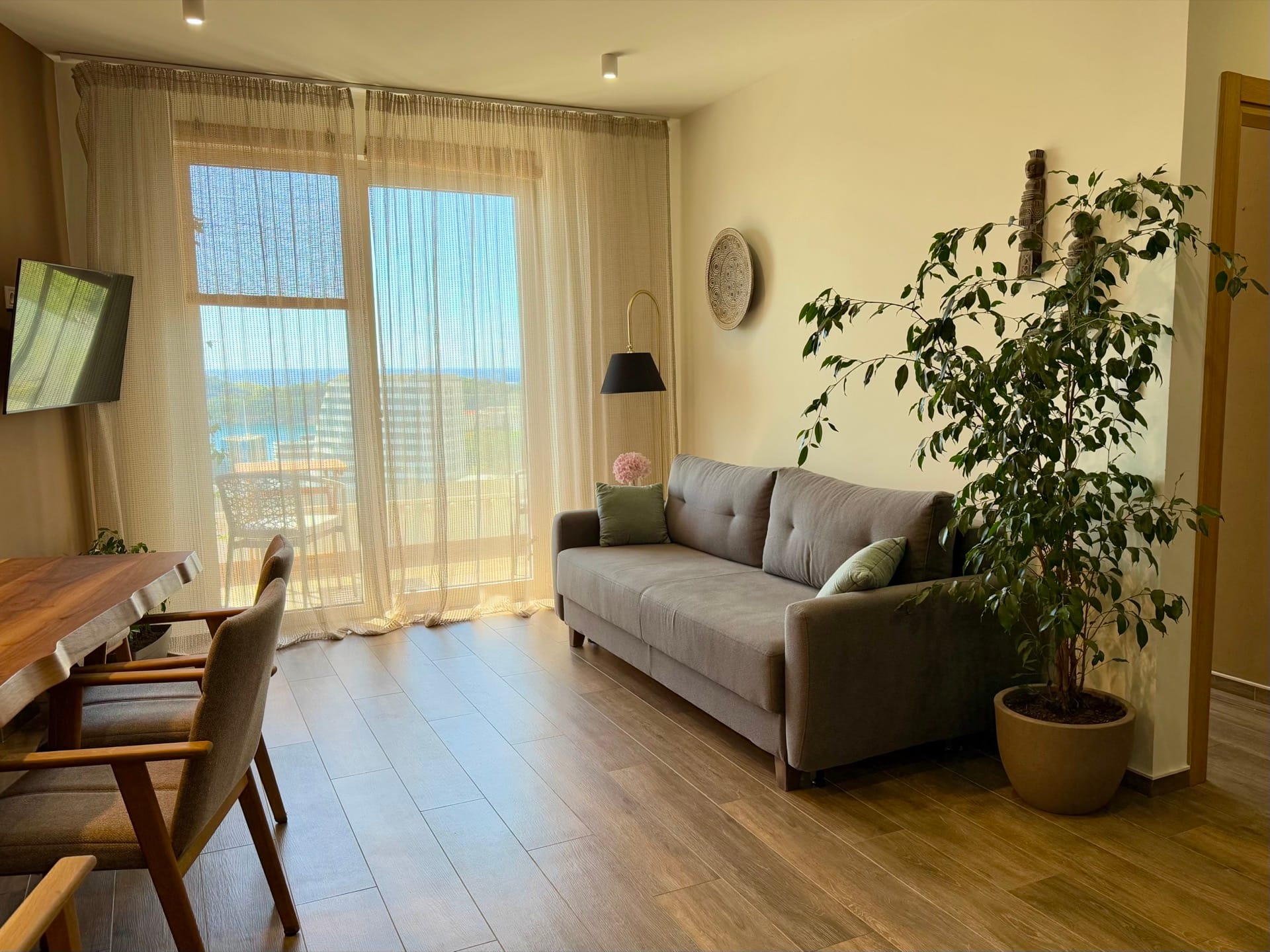 Dnevna soba u stanu u Bečićima, Crna Gora: siva sofa, sto od punog drveta i panoramski pogled na more sa terase.