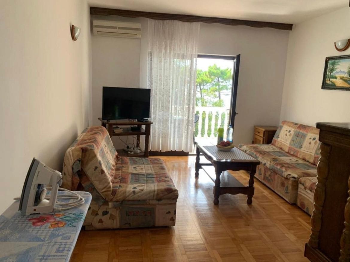 Dnevna soba u stanu na Svetom Stefanu, Crna Gora: dva kauča, drveni pod, izlaz na balkon s pogledom na borove.