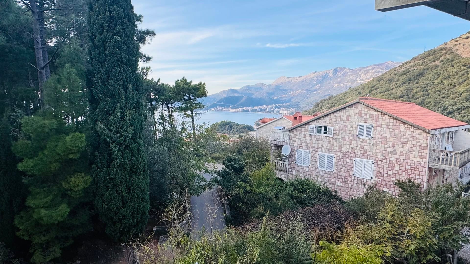Pogled na more i planine iz stana u Svetom Stefanu, Crna Gora: kamena kuća sa krovom od crepa i zelena bašta.