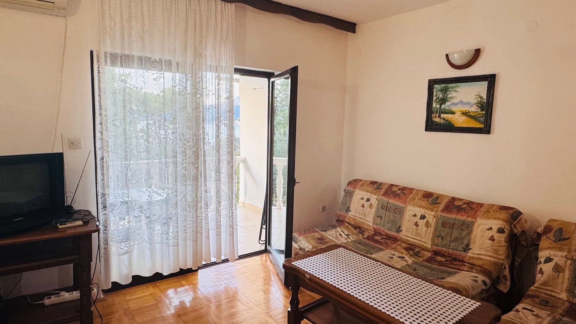 Dnevna soba u stanu na Svetom Stefanu, Crna Gora: sofa, drveni stočić, izlaz na balkon s pogledom na more.