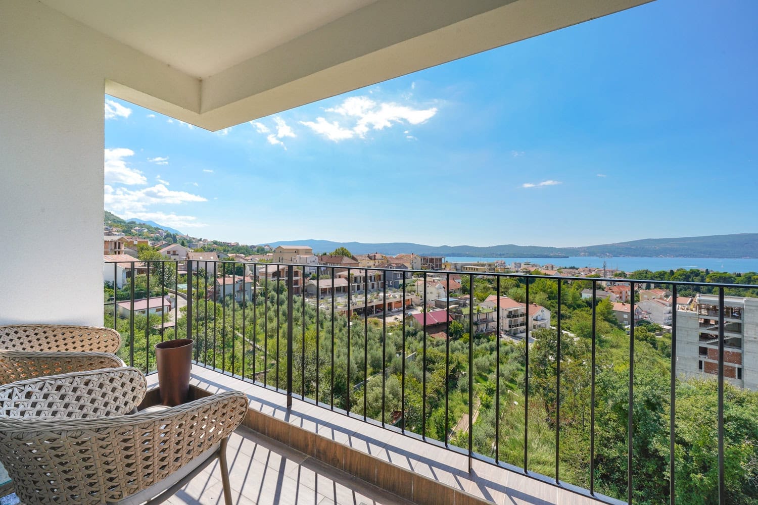 Balkon sa pletenim nameštajem i panoramskim pogledom na more i grad Tivat, Crna Gora. Sunčana terasa sa ogradom.