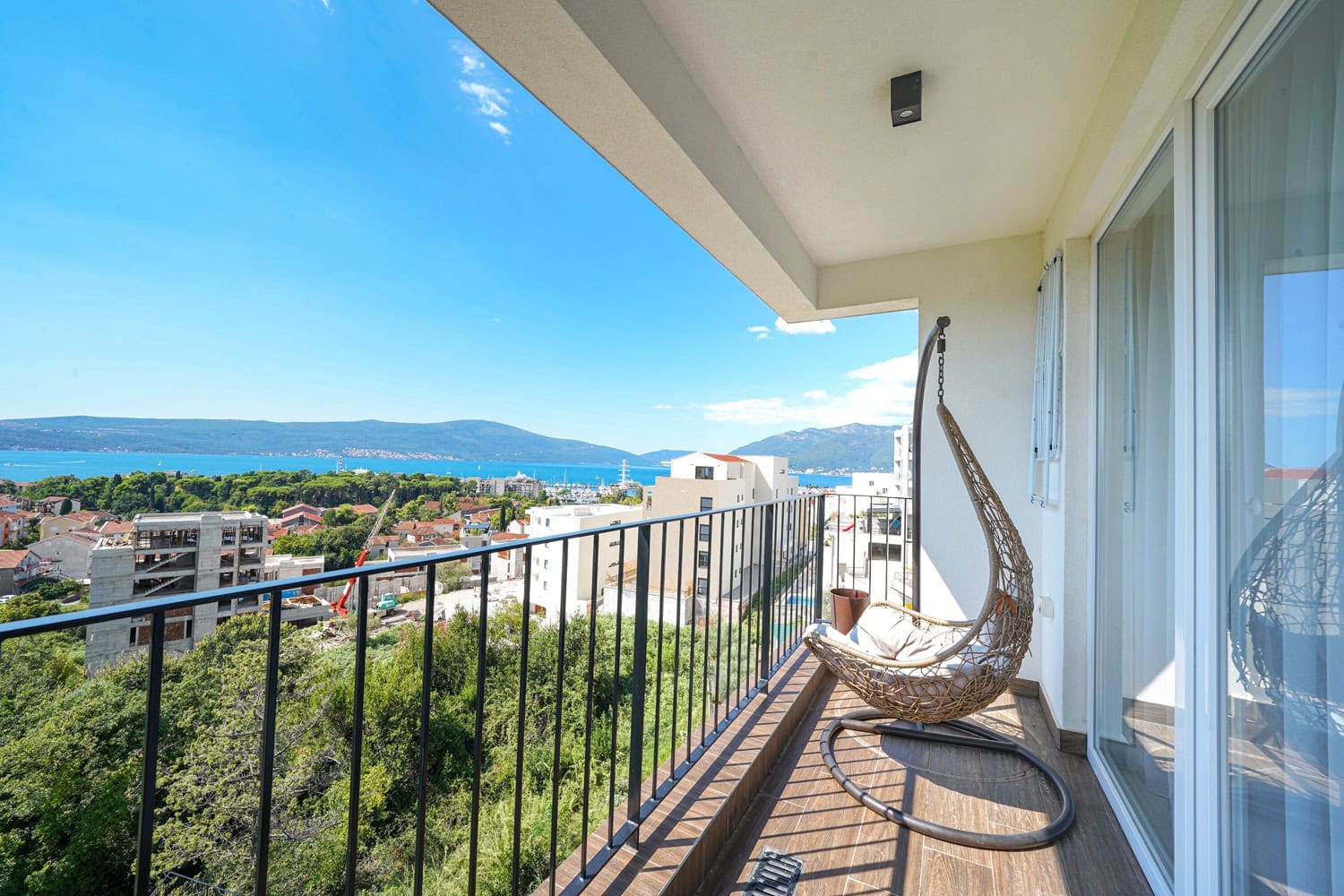 Balkon sa pletenom visećom foteljom i panoramskim pogledom na more i planine u stanu, grad Tivat, Crna Gora.
