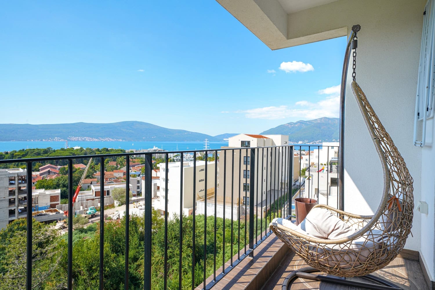 Balkon sa pletenom visećom foteljom i panoramskim pogledom na more i planine u stanu, grad Tivat, Crna Gora.