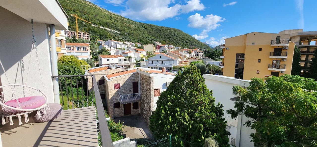 View from the townhouse balcony in Petrovac, Montenegro: a hanging chair, green mountains, and city buildings.