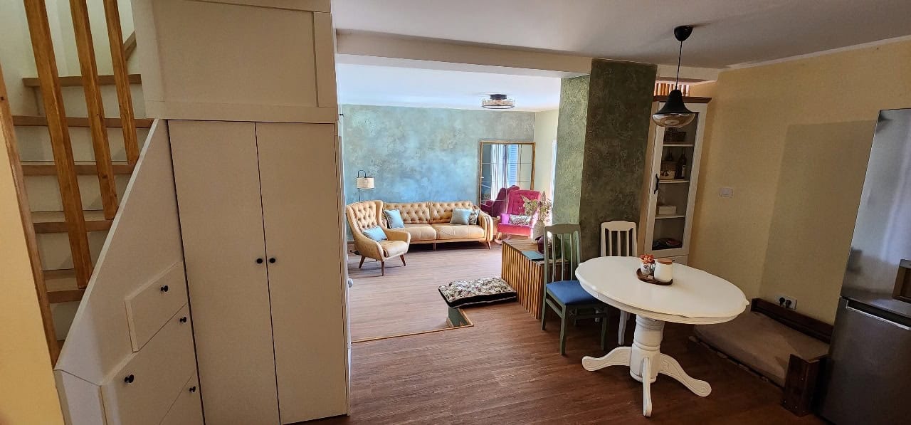 Living room interior in a townhouse, Petrovac, Montenegro: dining area, staircase, and soft furnishings in light tones.