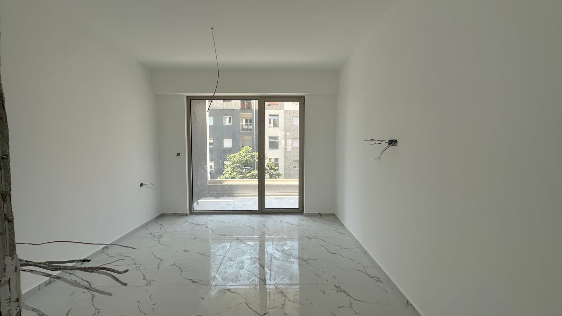 Dnevna soba u novogradnji u Budvi, Crna Gora: svetla završna obrada, pod od porcelanskog pločica u imitaciji mermera, izlaz na balkon.