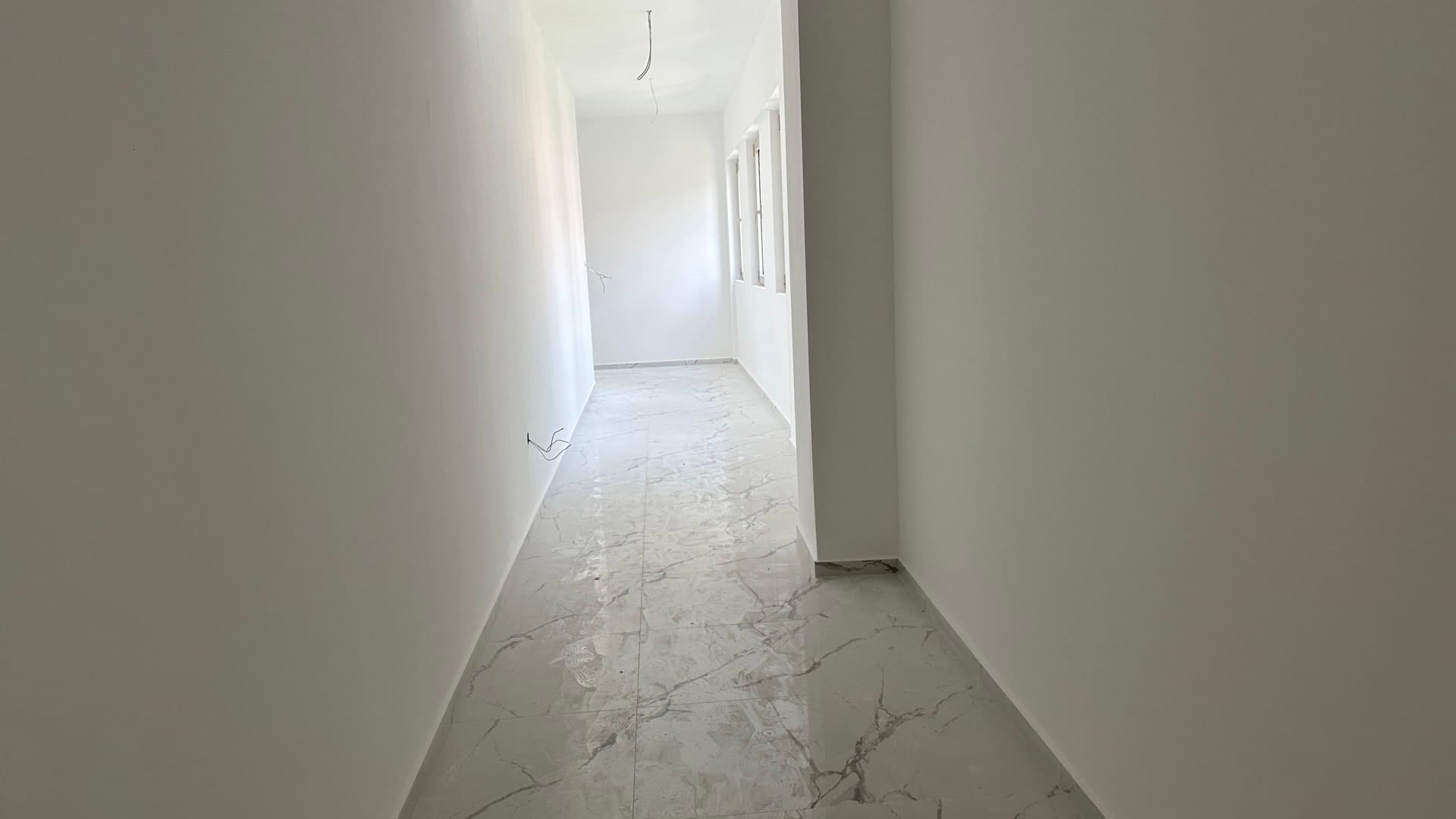 Svetao hodnik u novom stanu u Budvi, Crna Gora: beli zidovi i pod od keramičkih pločica u imitaciji mermera, predzavršna obrada.
