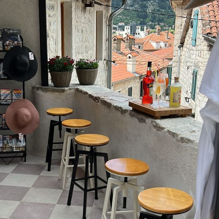 Balkon kuće u Kotoru, Crna Gora: barske stolice, kamena obloga i panoramski pogled na stari grad i krovove od crepova.