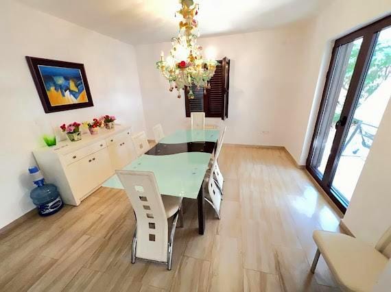 Svetao dnevni boravak sa trpezarijskim delom u vili u Budvi, Crna Gora: stakleni sto, kristalni luster i panoramski prozori.