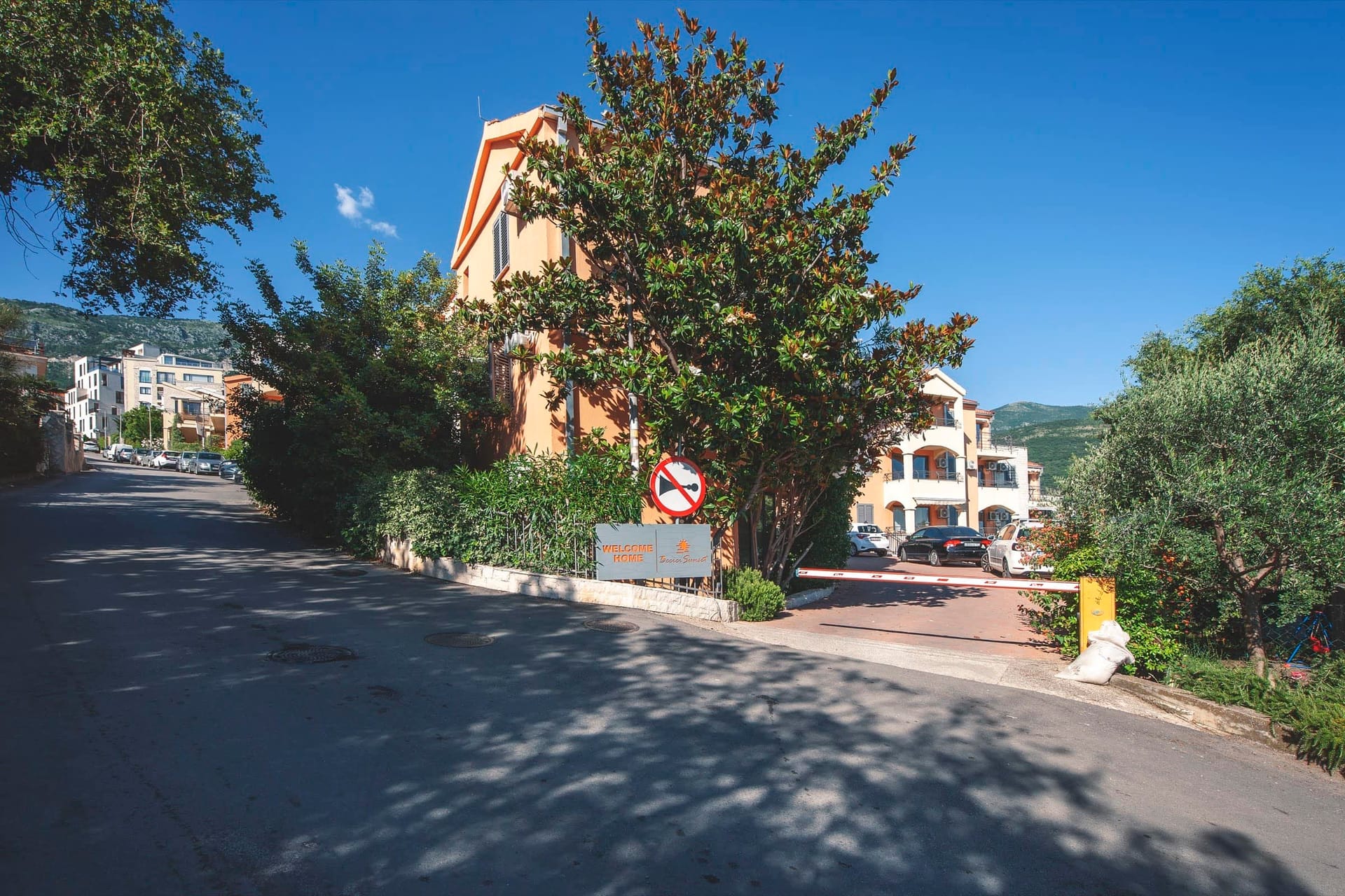 Fasada stambenog kompleksa sa parkingom i ulazom u Bečiće, Crna Gora: pogled na zgradu sa zelenom površinom i rampom.