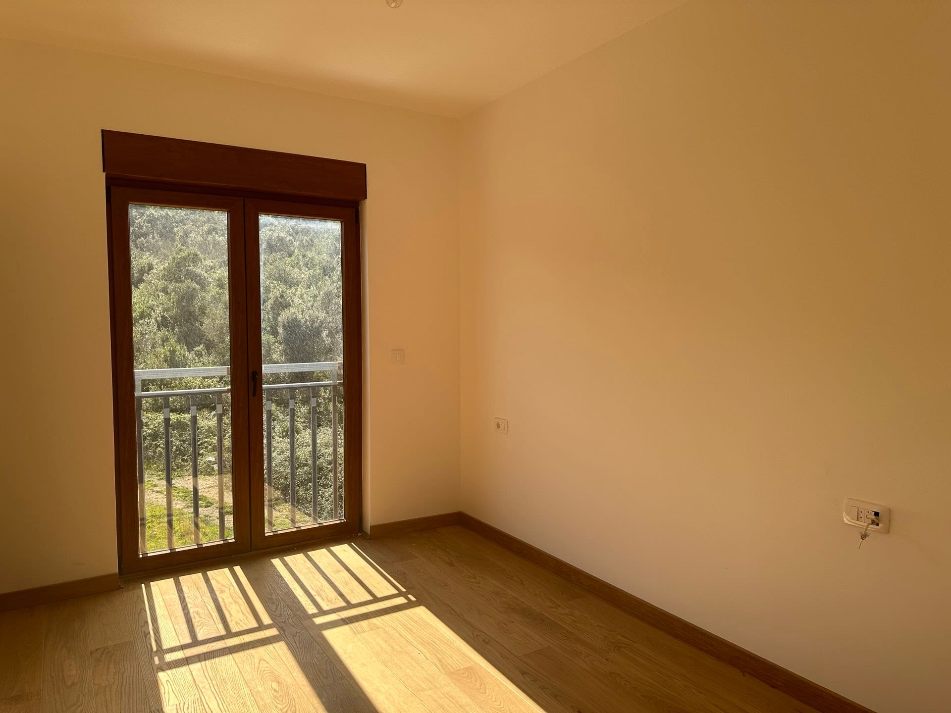 Svetla spavaća soba sa parketom i izlazom na balkon u stanu u Krašićima, Crna Gora, pogled na zelenu šumsku masu.