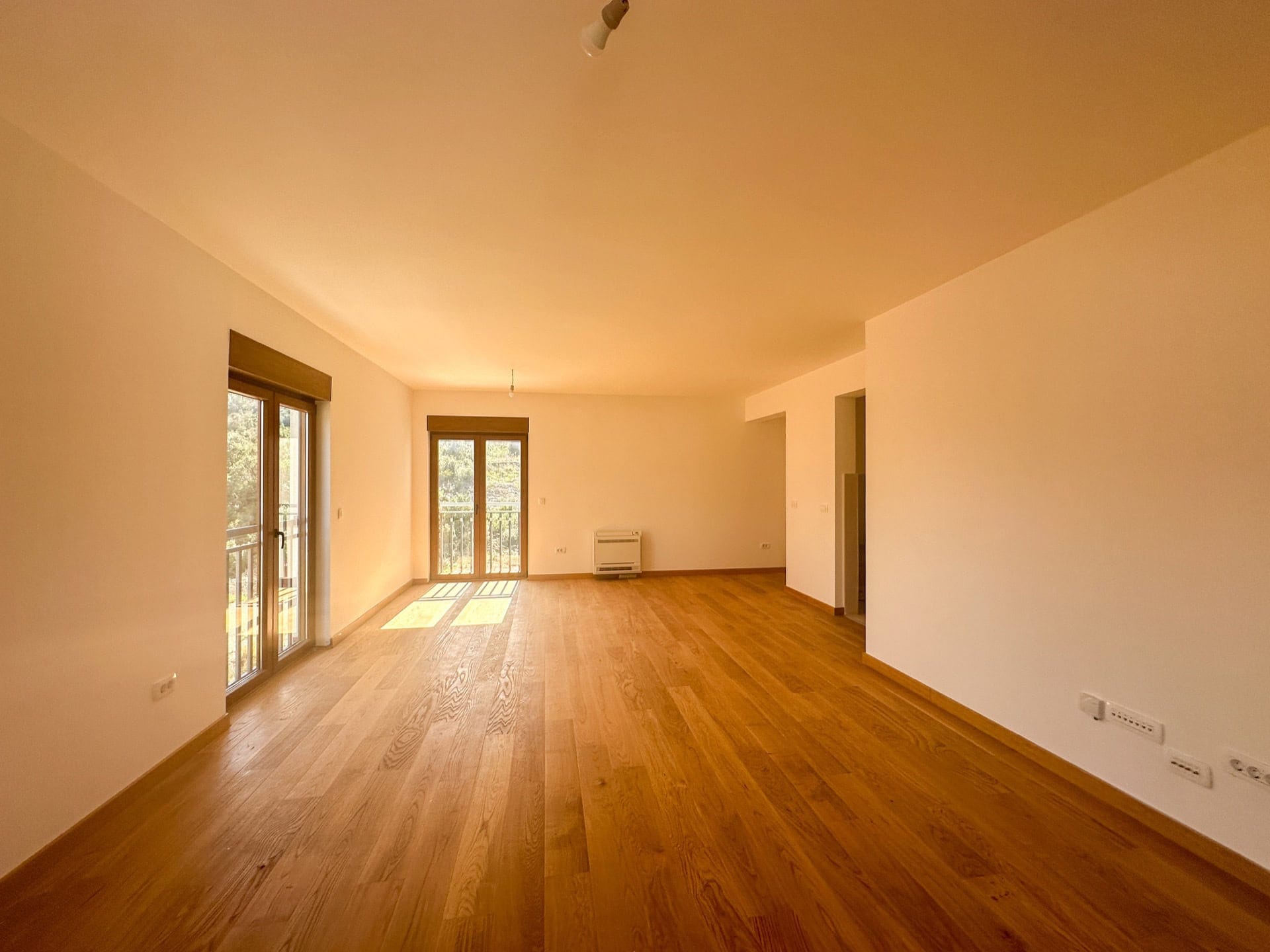 Svetla dnevna soba sa parketnim podom i izlazom na balkon u stanu, Krašići, Crna Gora.