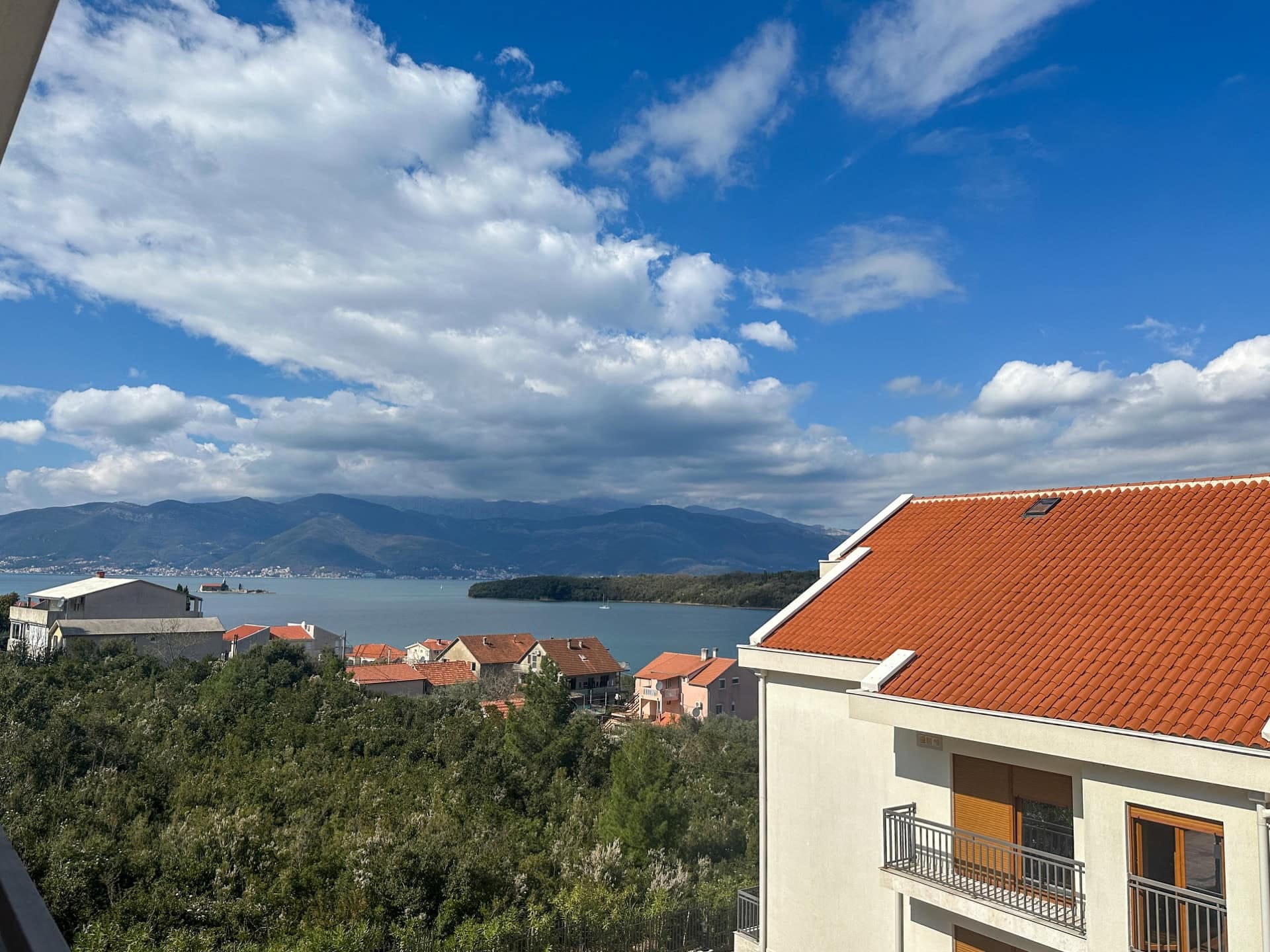 Pogled s balkona na more, planine i krovove od crepa u naselju Krašići, Crna Gora. Panorama zaliva i stambenog kompleksa.