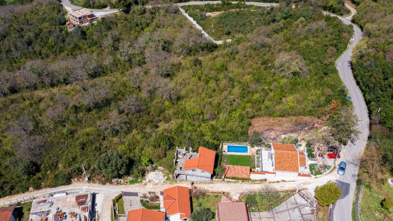 Land plot in Kavac, Montenegro: aerial view of a house with a pool and the surrounding grounds amid greenery.