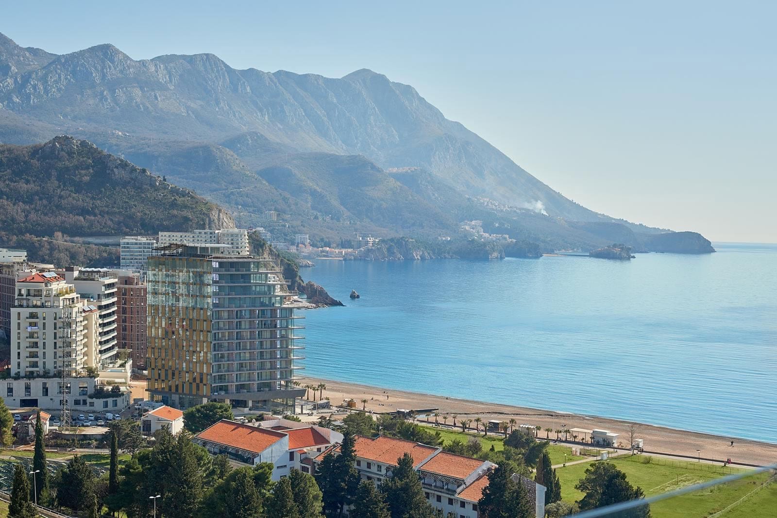 Panoramablick auf das Meer, den Strand und die Berge in Bečići, Montenegro, mit modernen Wohnanlagen an der Küste.