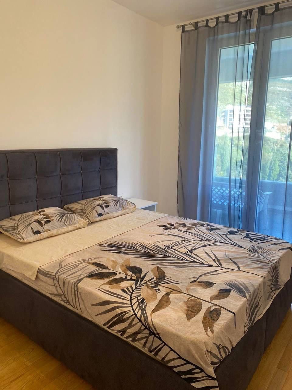 Schlafzimmer mit Doppelbett und Zugang zum Balkon in einer Wohnung, Becici, Montenegro. Moderne Möbel, helles Interieur.