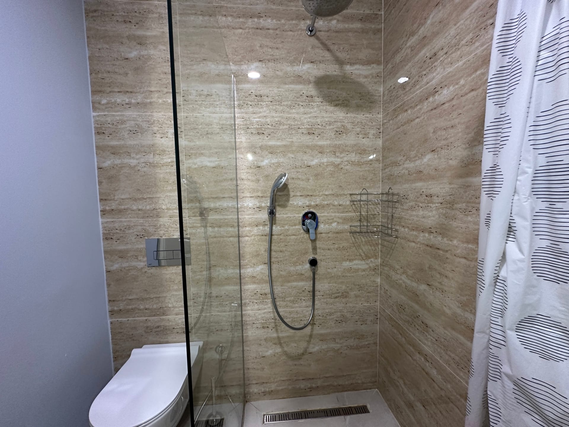 Modernes Badezimmer mit Duschkabine und Travertinoptik in einer Wohnung, Bečići, Montenegro.