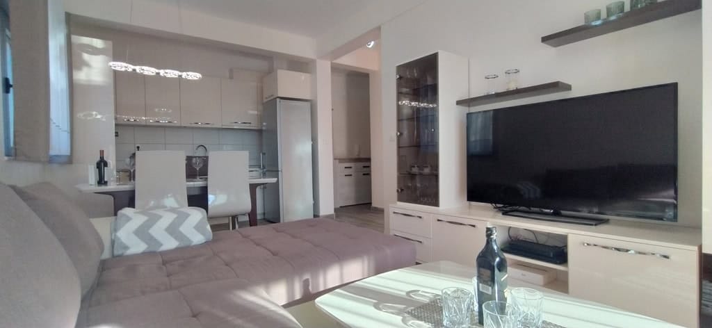 Moderna dnevna soba sa kuhinjom u stanu u Bečićima, Crna Gora: ugaona sofa, TV zona i trpezarijski nameštaj.