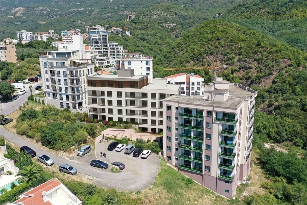 Pogled iz vazduha na moderne stambene komplekse u Bečićima, Crna Gora, sa parkingom i planinskim pejzažom u pozadini.