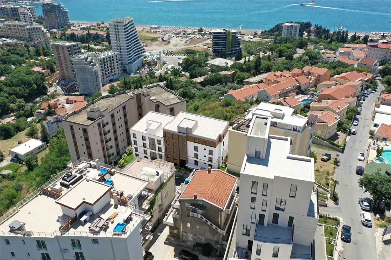 Pogled iz vazduha na moderne stambene komplekse u Bečićima, Crna Gora, sa panoramskim pogledom na more i plažu.