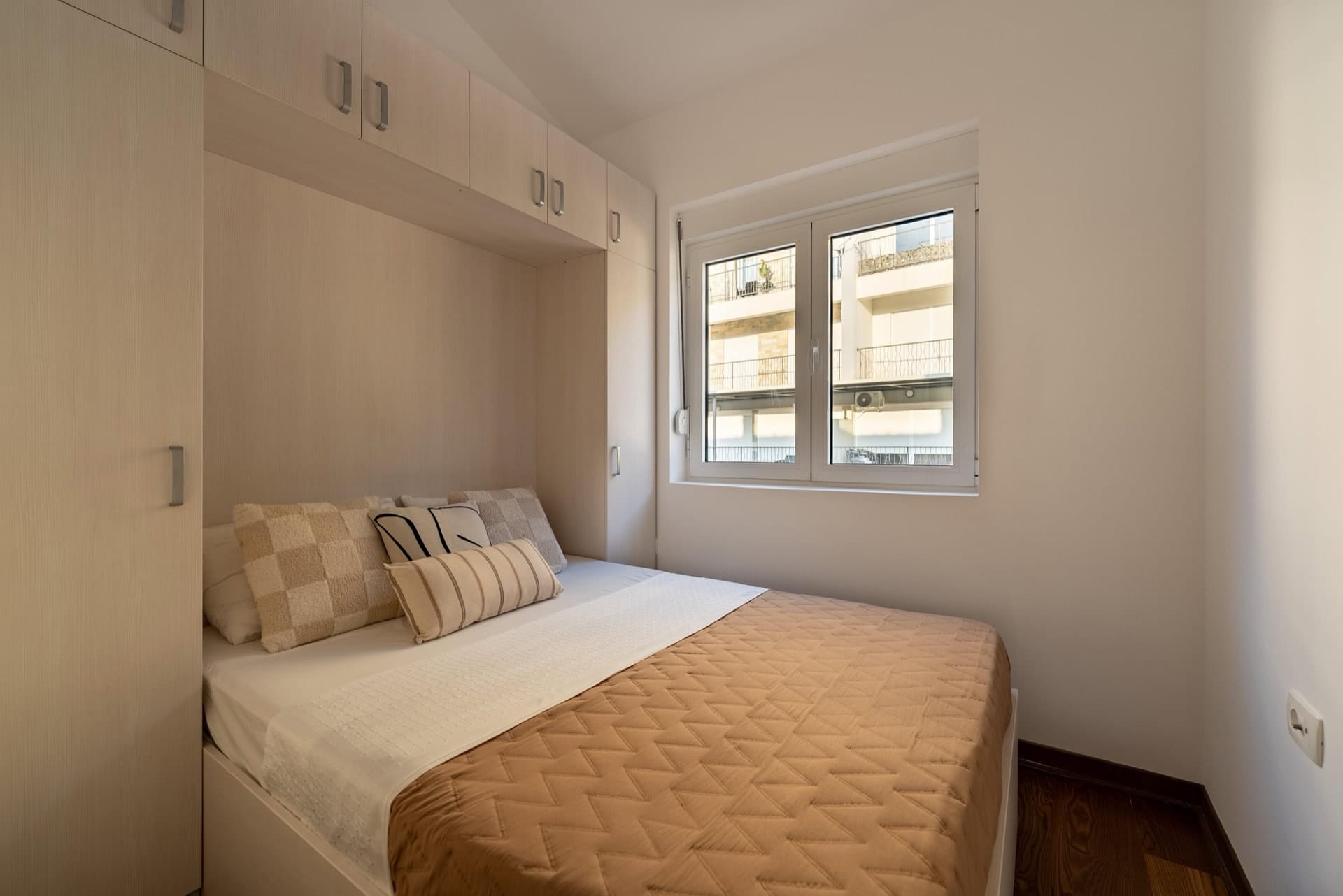 Schlafzimmer in einer Wohnung in Pržno, Montenegro: Doppelbett, heller Einbauschrank und Fenster mit Blick auf die Stadt.