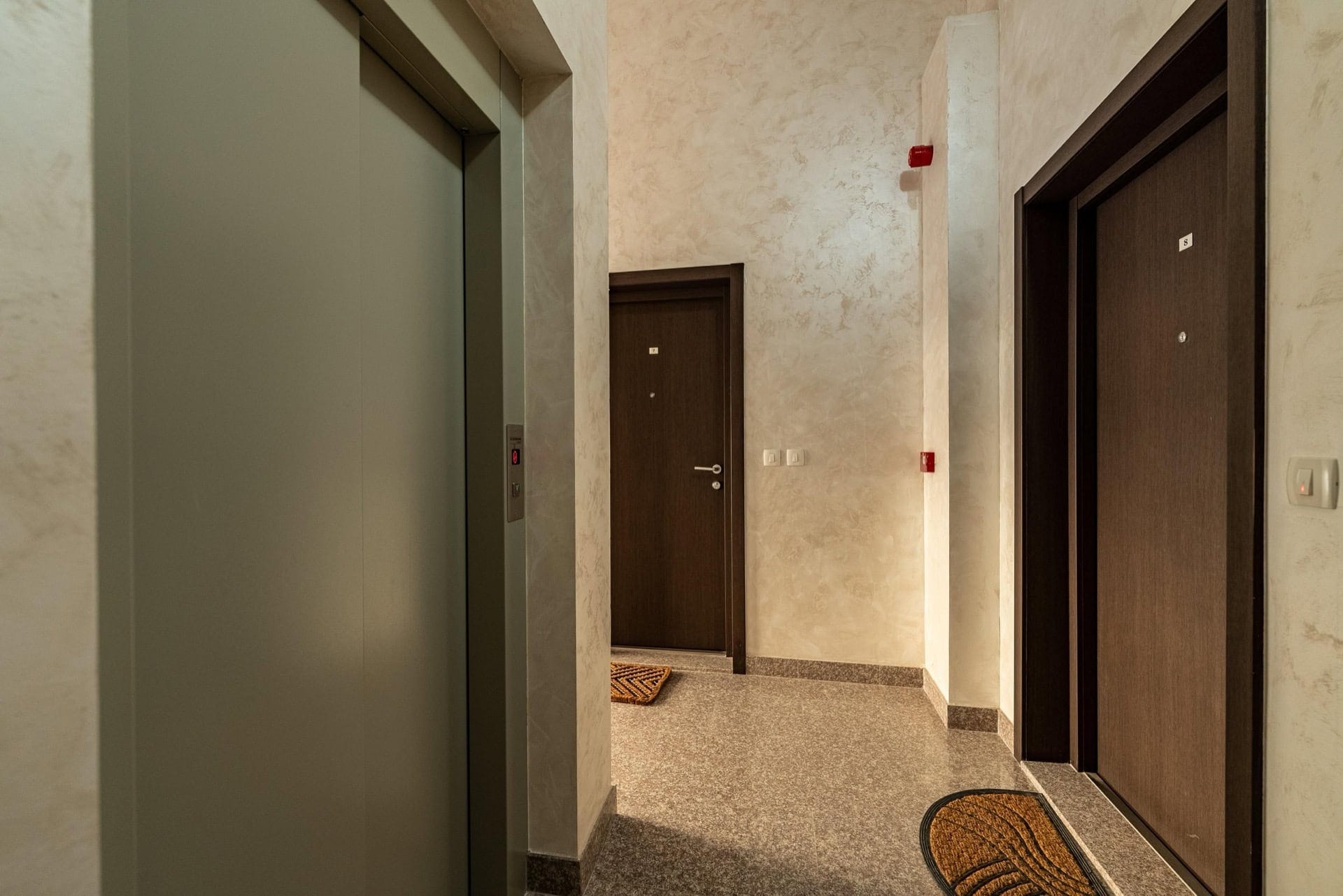Moderner Hauseingang mit Aufzug und Wohnungstüren in einer Wohnanlage, Pržno, Montenegro: helle Wandverkleidung und Fliesen.