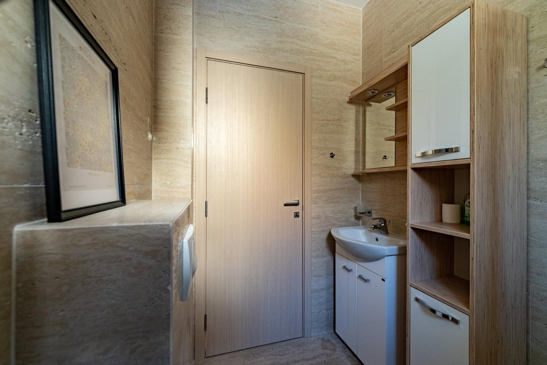 Modernes Badezimmer in einer Wohnung in Pržno, Montenegro: weiße Möbel, Spiegel und Verkleidung aus hellem Stein.