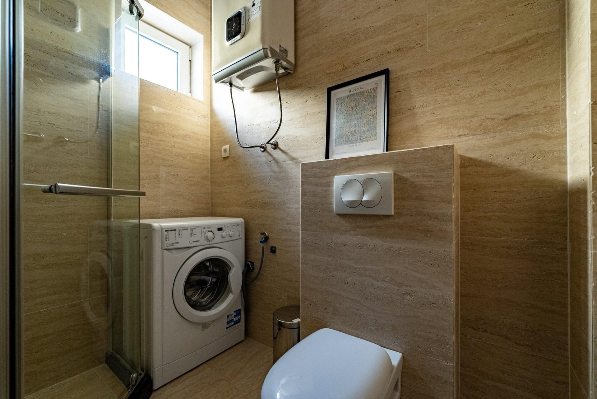 Badezimmer in einer Wohnung in Pržno, Montenegro: Duschkabine, Waschmaschine, Vorwandinstallation und beige Fliesen.