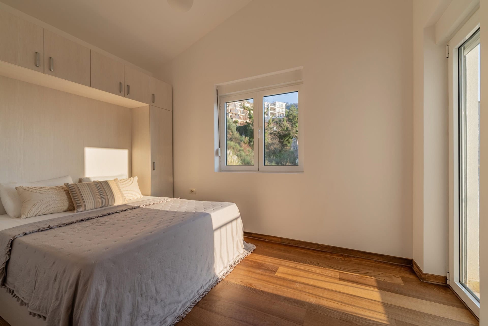 Helles Schlafzimmer mit Doppelbett und Einbauschrank in einer Wohnung in Pržno, Montenegro, mit Bergblick.