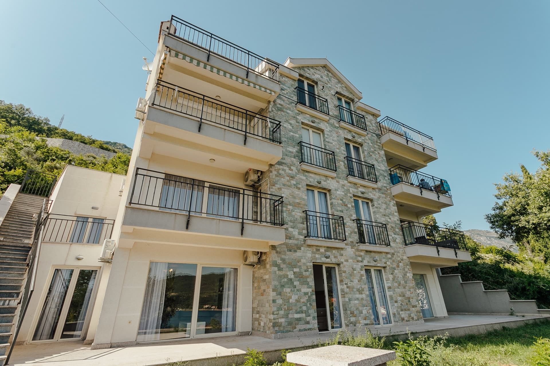 Fassade eines modernen Wohnhauses mit Steinverkleidung und Balkonen in Kamenari, Montenegro.