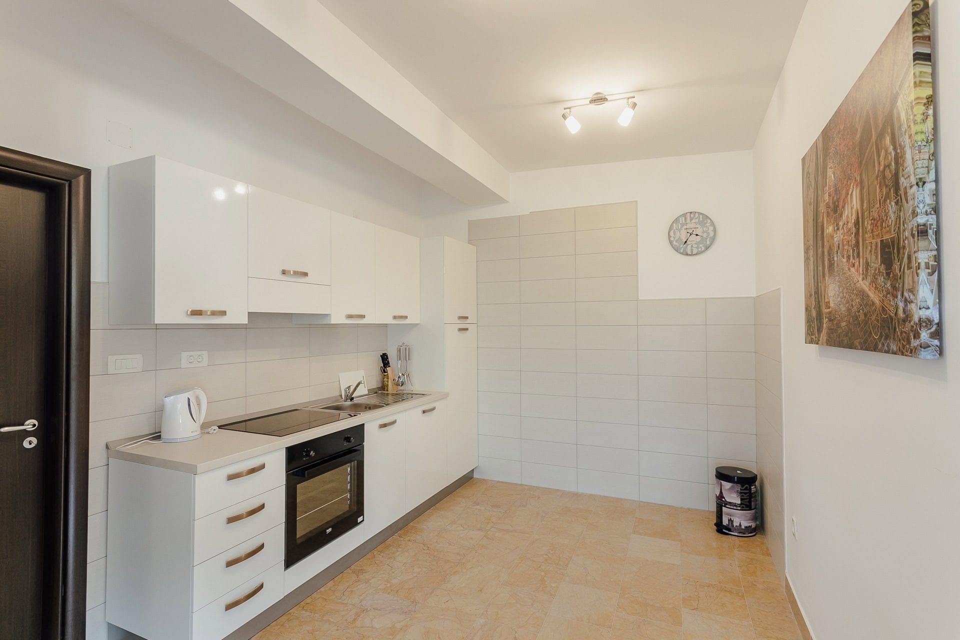 Moderne weiße Küche in einer Wohnung in Kamenari, Montenegro: Einbaugeräte, Fliesenboden und helles Interieur.