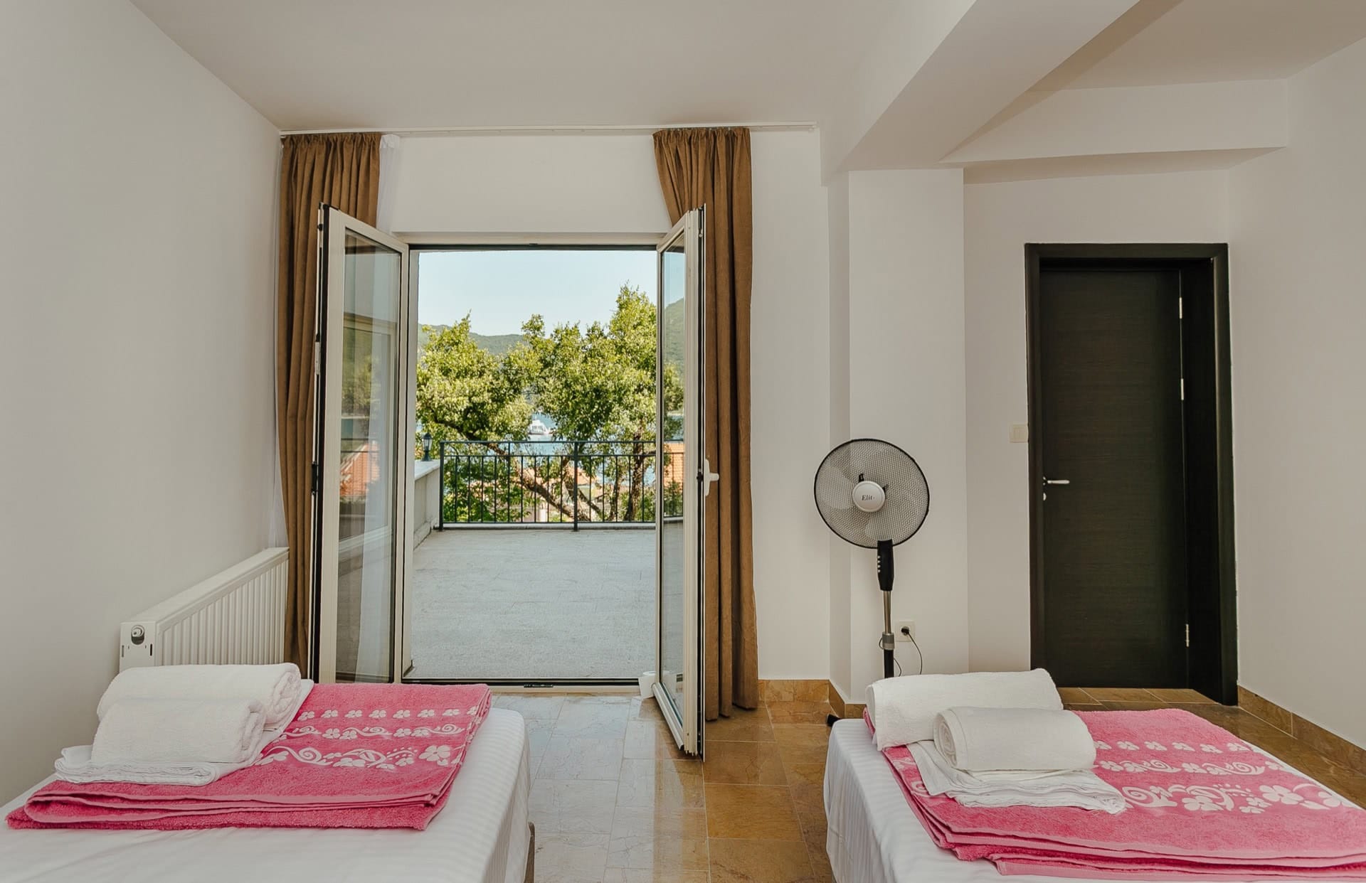 Schlafzimmer in einer Wohnung in Kamenari, Montenegro: zwei Betten, Zugang zur Terrasse mit Blick auf Meer und Berge, helles Interieur.