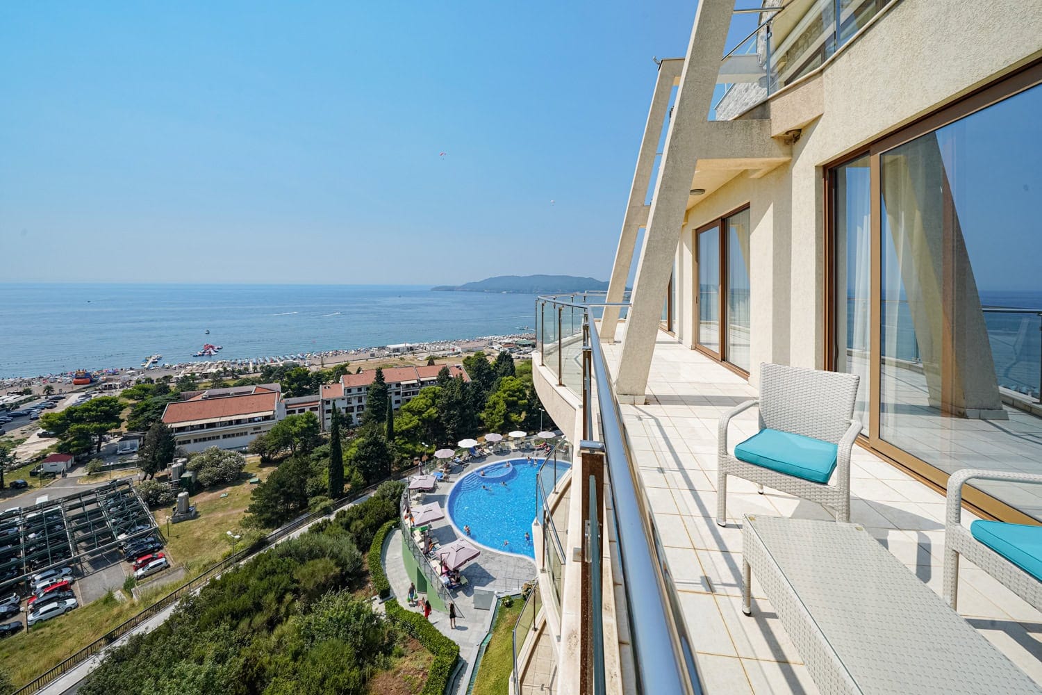 Balkon z plecionymi meblami i panoramicznym widokiem na morze, plażę i basen w kompleksie mieszkaniowym w Rafailovici, Czarnogóra.