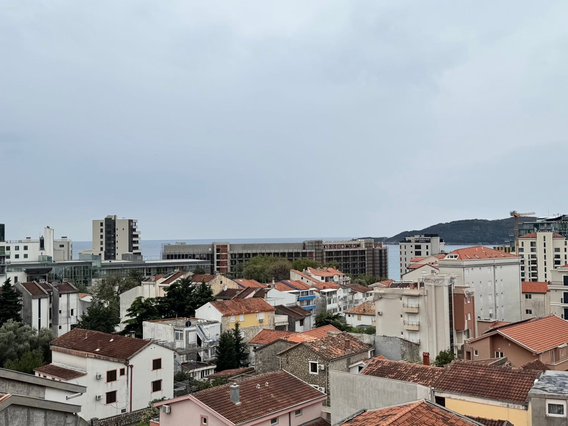 Panoramski pogled na grad Bečići, Crna Gora: stambene zgrade sa krovovima od crepa i morski horizont u daljini.
