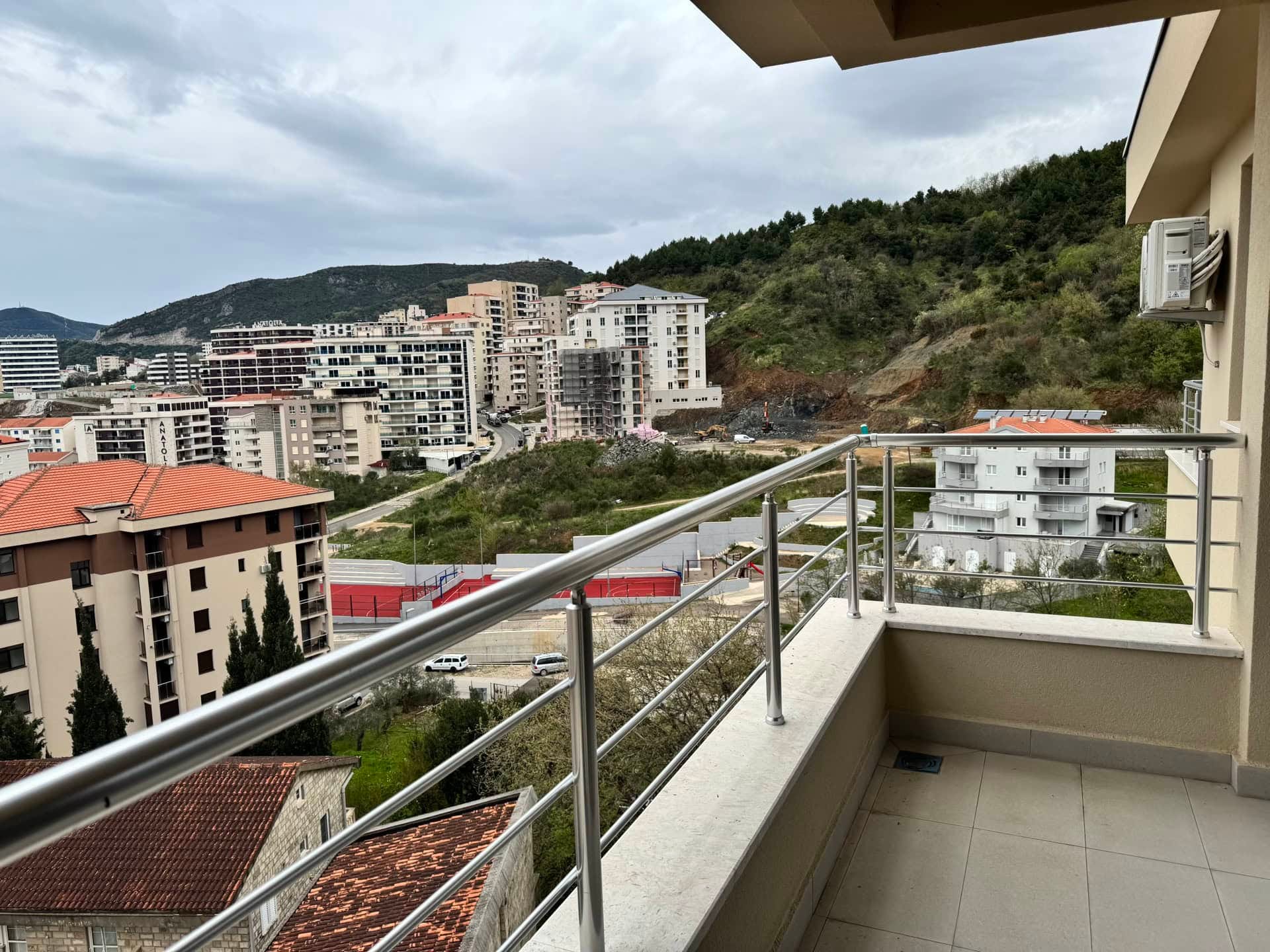 Karadağ, Bečići’deki dairenin balkonundan görünüm: şehir panoraması, modern konut kompleksleri ve arka planda dağlar.