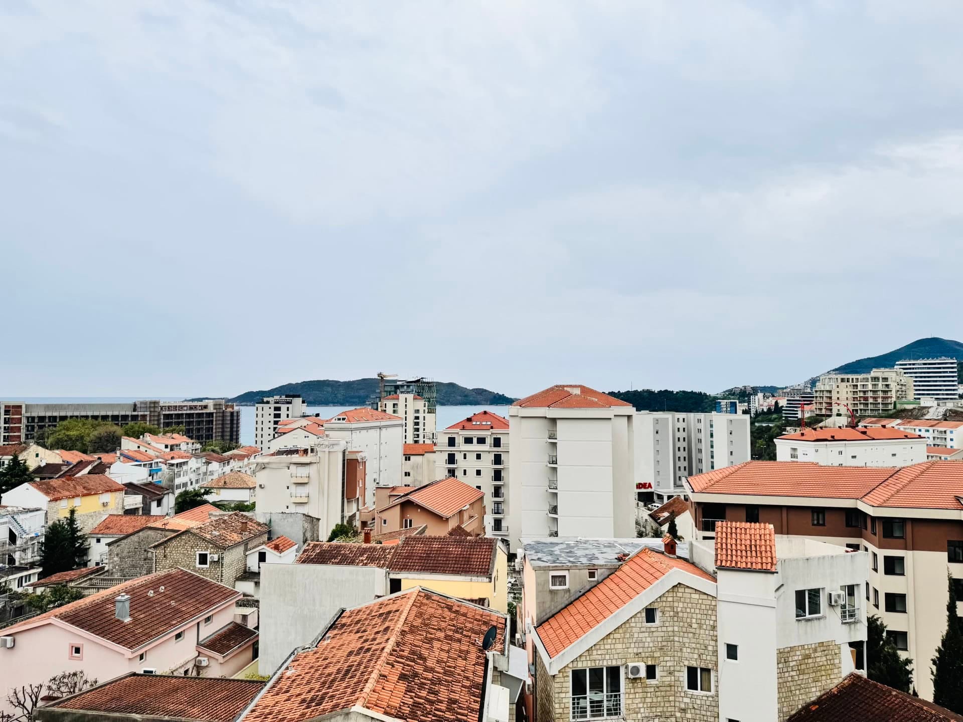 Karadağ, Bečići şehrinin panoramik manzarası; kırmızı kiremitli ev çatıları ve ufukta deniz kıyısı.