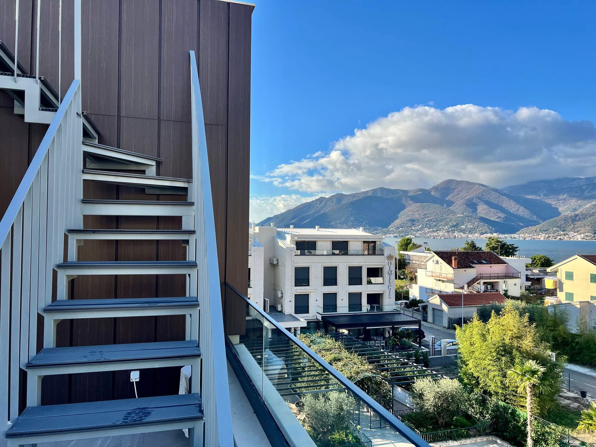 Pogled sa balkona stana u Tivtu, Crna Gora: moderno stepenište, panoramski pogled na more i planine Bokokotorskog zaliva.