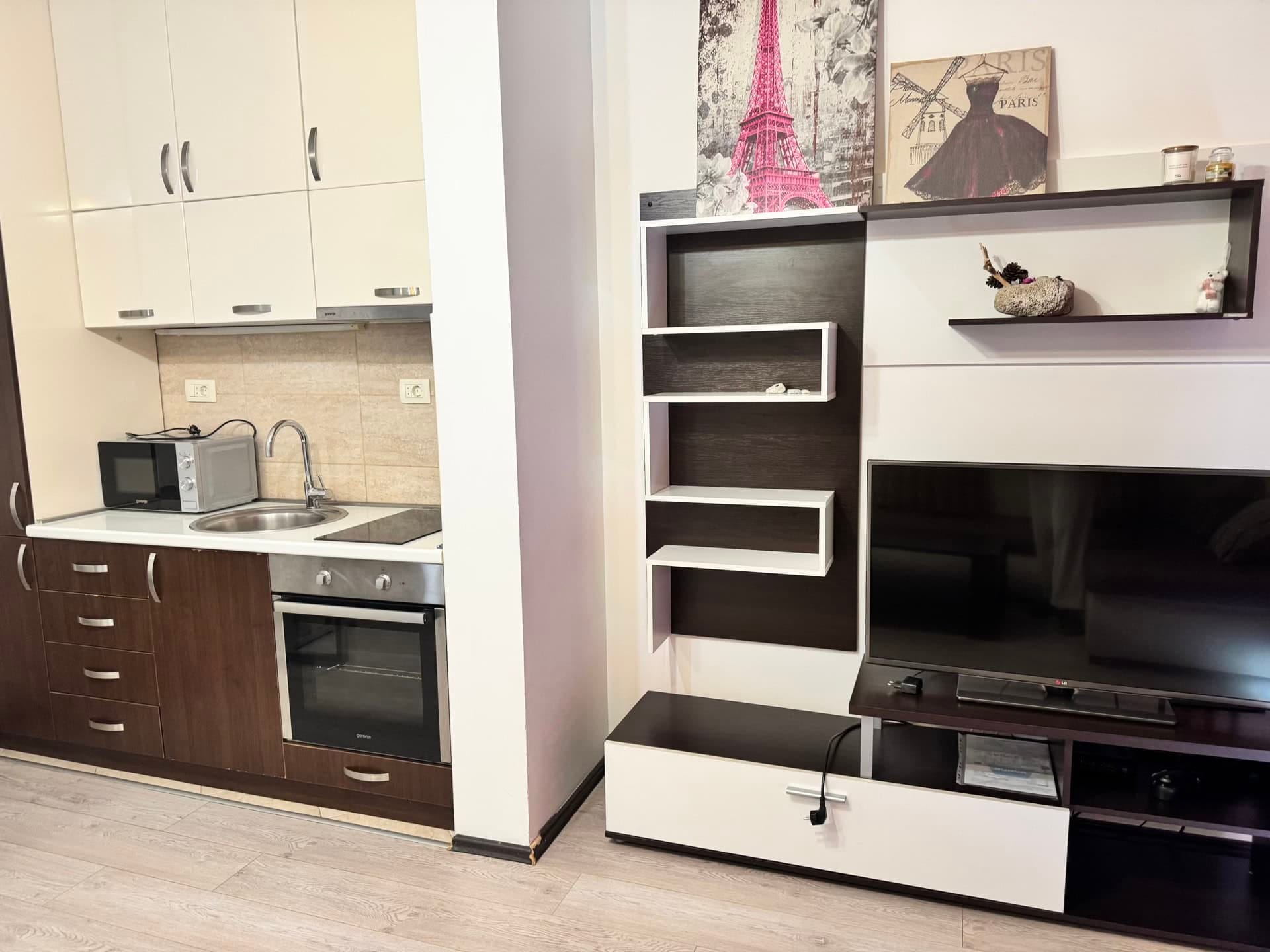 Kitchen-living room in an apartment in Budva, Montenegro: modern kitchen set, built-in appliances, and a TV area with shelves.