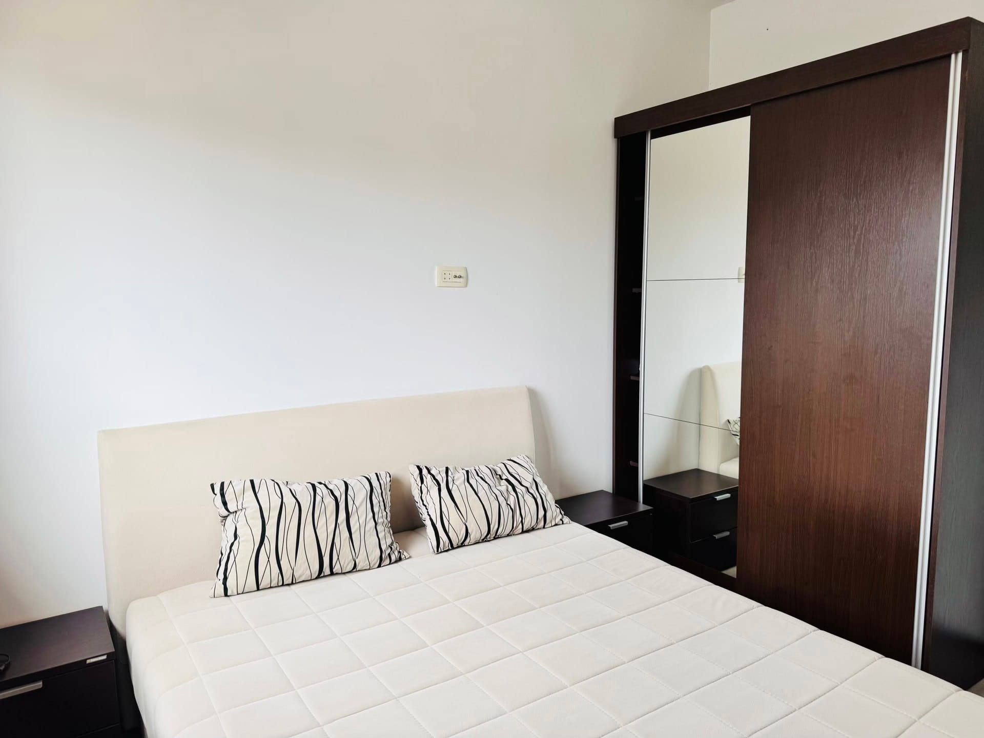 Bedroom in an apartment in Budva, Montenegro: a double bed with a white headboard and a mirrored sliding wardrobe.