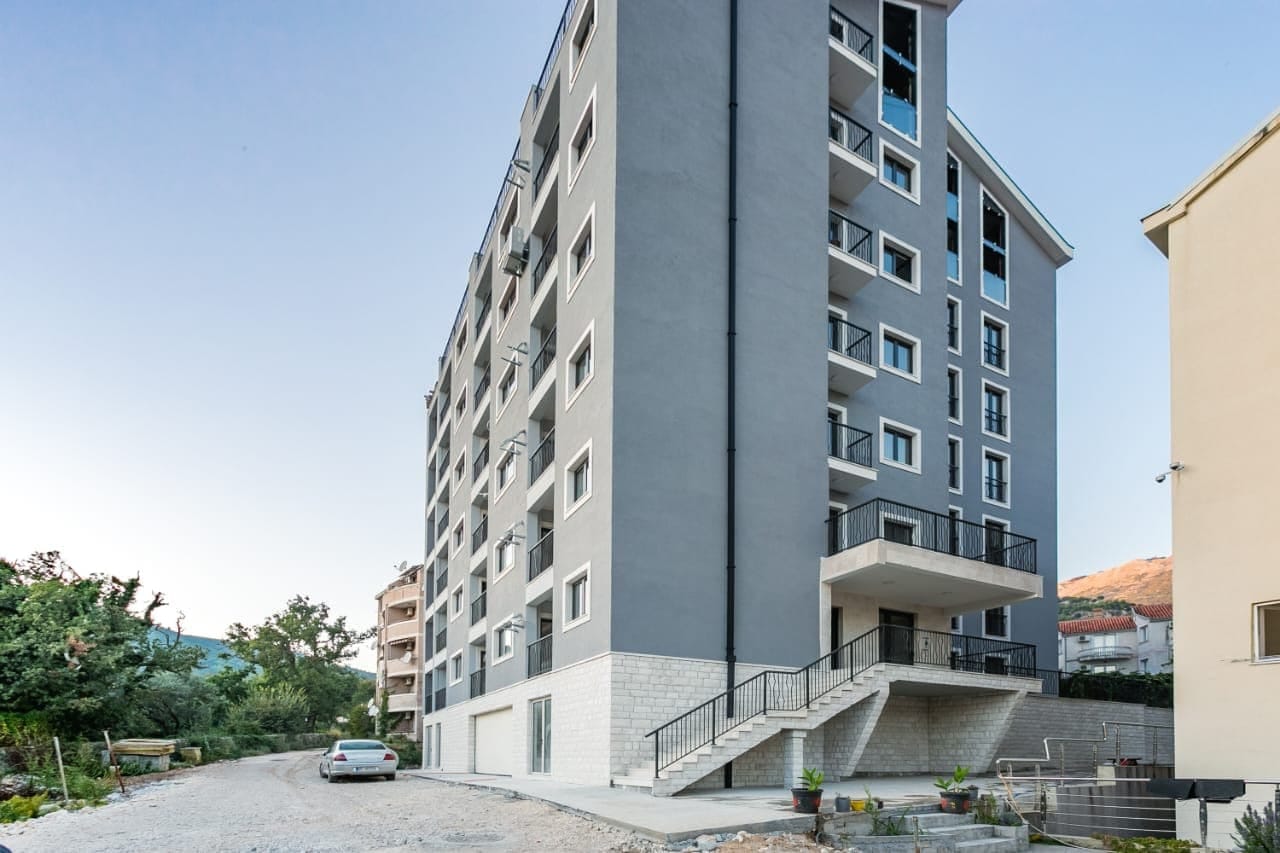 Modern residential complex with gray facade finishing in Budva, Montenegro: view of the building and surrounding area.