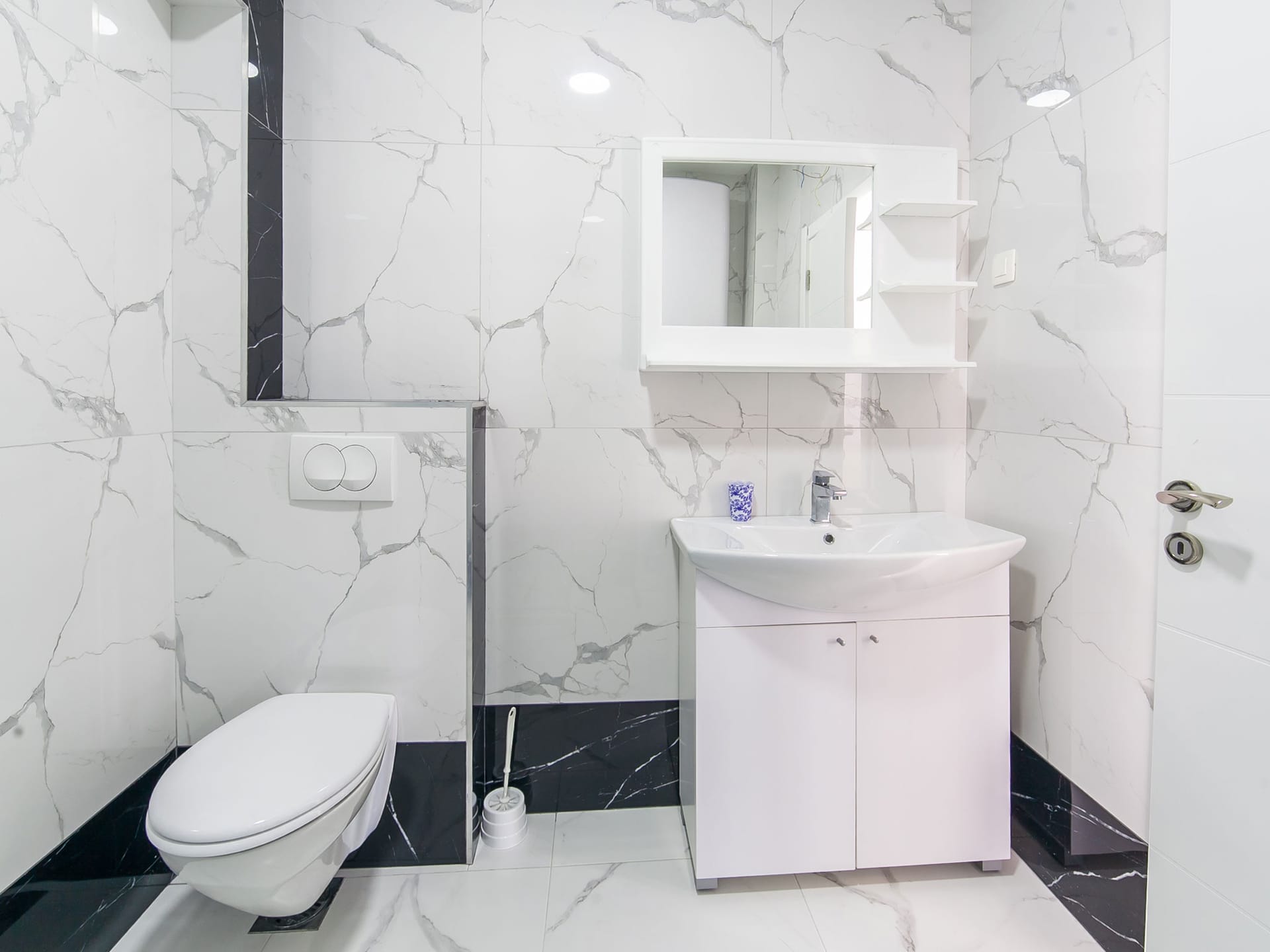 Modern bathroom with marble-style finishes in an apartment in Bečići, Montenegro: wall-mounted toilet and vanity with sink.