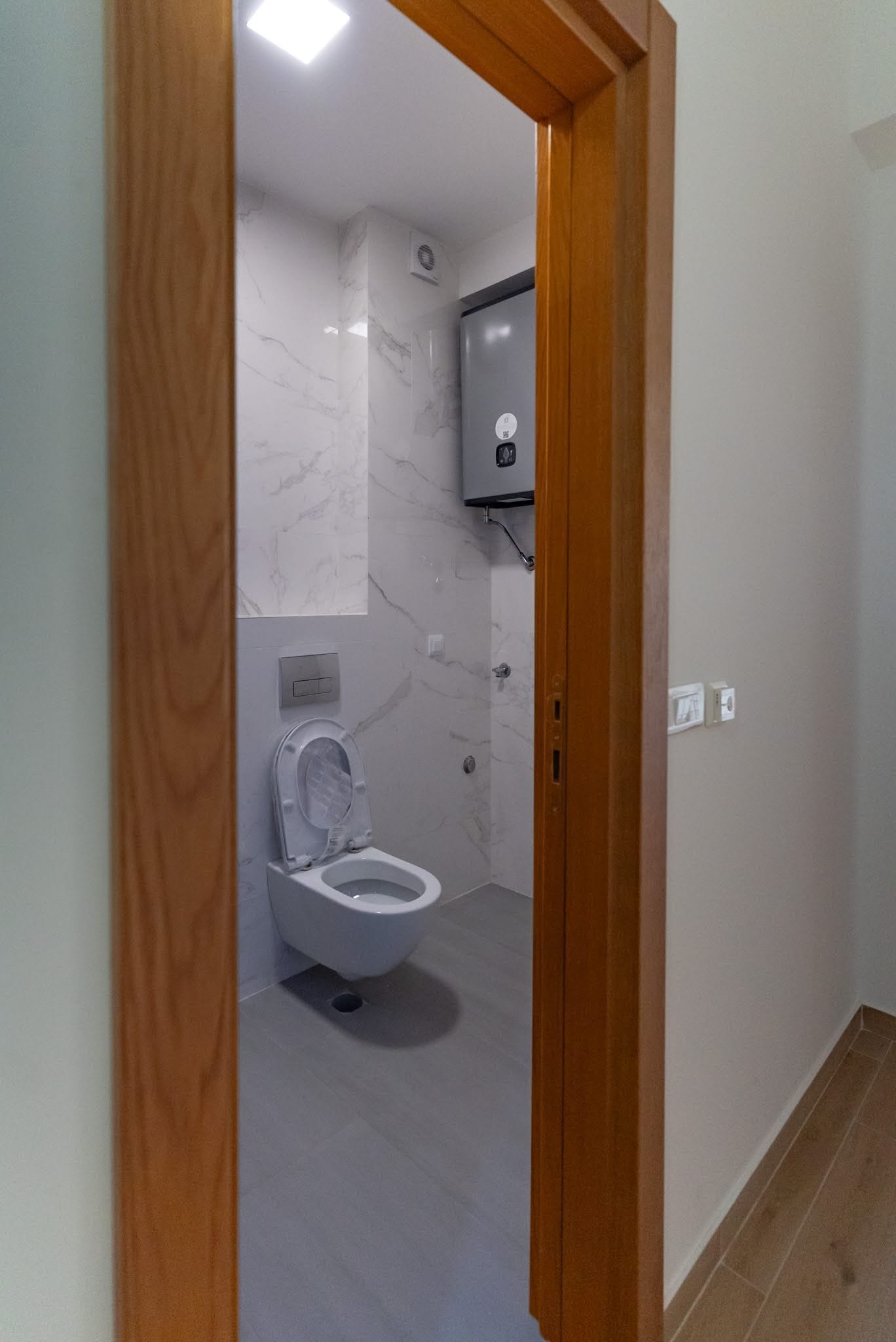 Karadağ, Budva’daki dairede modern banyo: asma klozet, mermer görünümlü fayans kaplama ve бойлер.