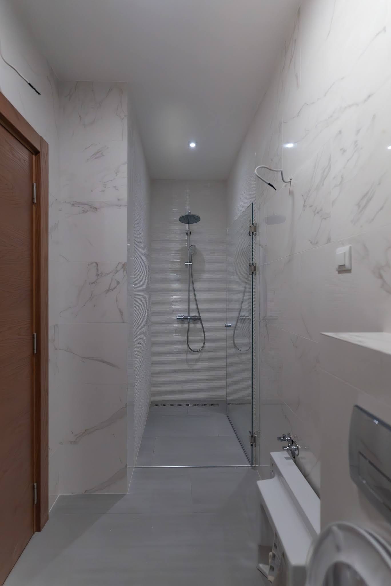 Karadağ, Budva’daki bir dairede modern banyo: tropik duşlu duş kabini ve mermer görünümlü fayans kaplama.