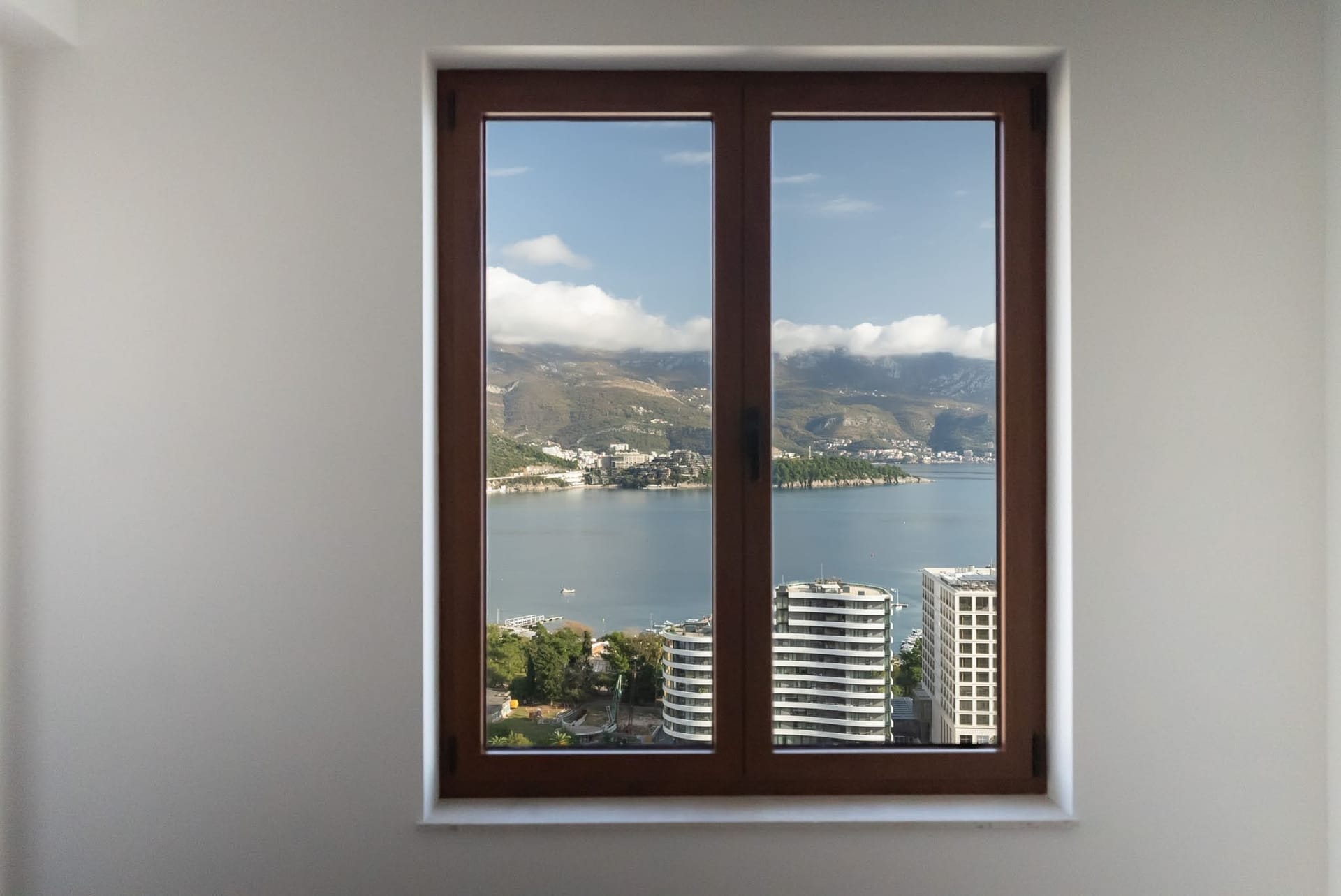 Budva, Karadağ’daki dairede oturma odası penceresinden deniz ve dağ manzarası: modern camlama ve panoramik peyzaj.