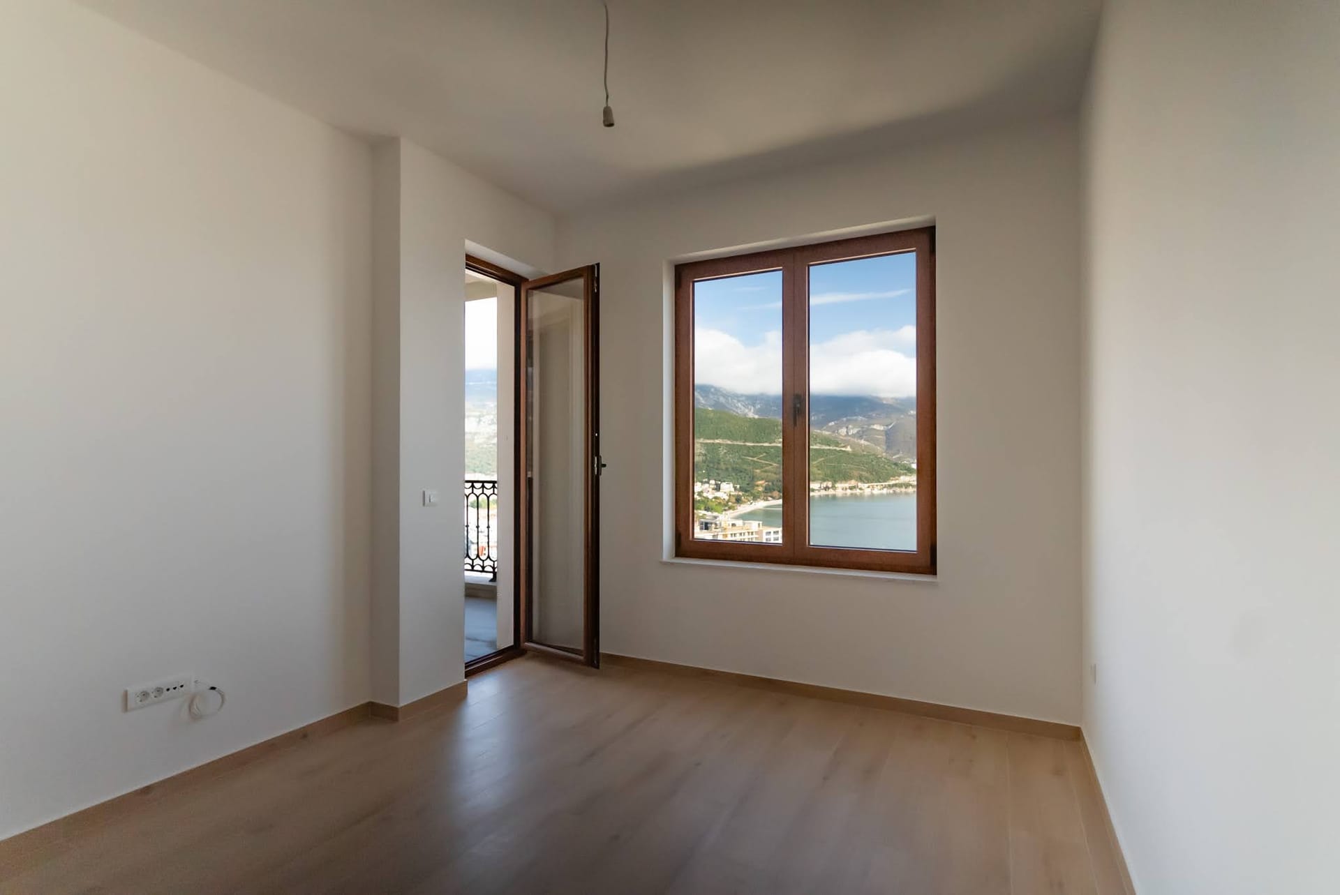 Budva, Karadağ’da balkon çıkışlı, deniz ve dağların panoramik manzarasına sahip, temiz bitişli aydınlık yatak odası.