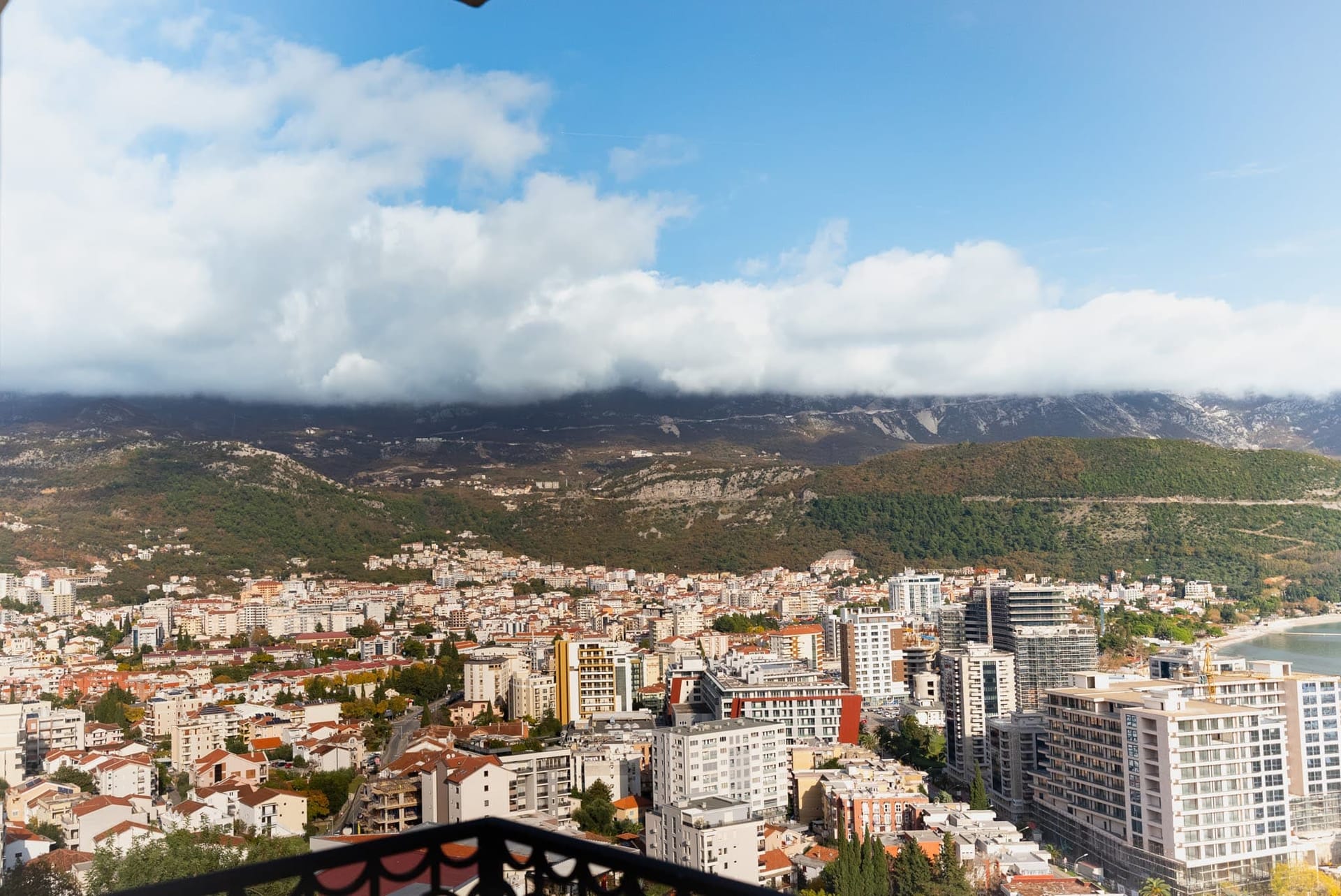 Karadağ’daki dairenin balkonundan Budva şehri ve dağların panoramik manzarası, konut mahalleleri ve deniz kıyısı görünümü.