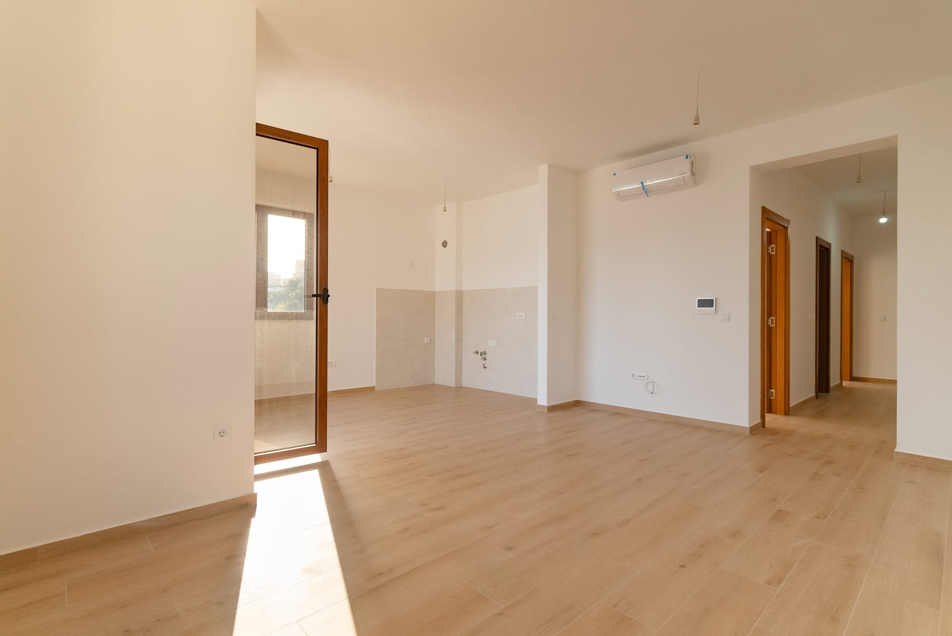 Svetao dnevni boravak u novom stanu u Budvi, Crna Gora: laminat, beli zidovi, klima-uređaj i izlaz na balkon.