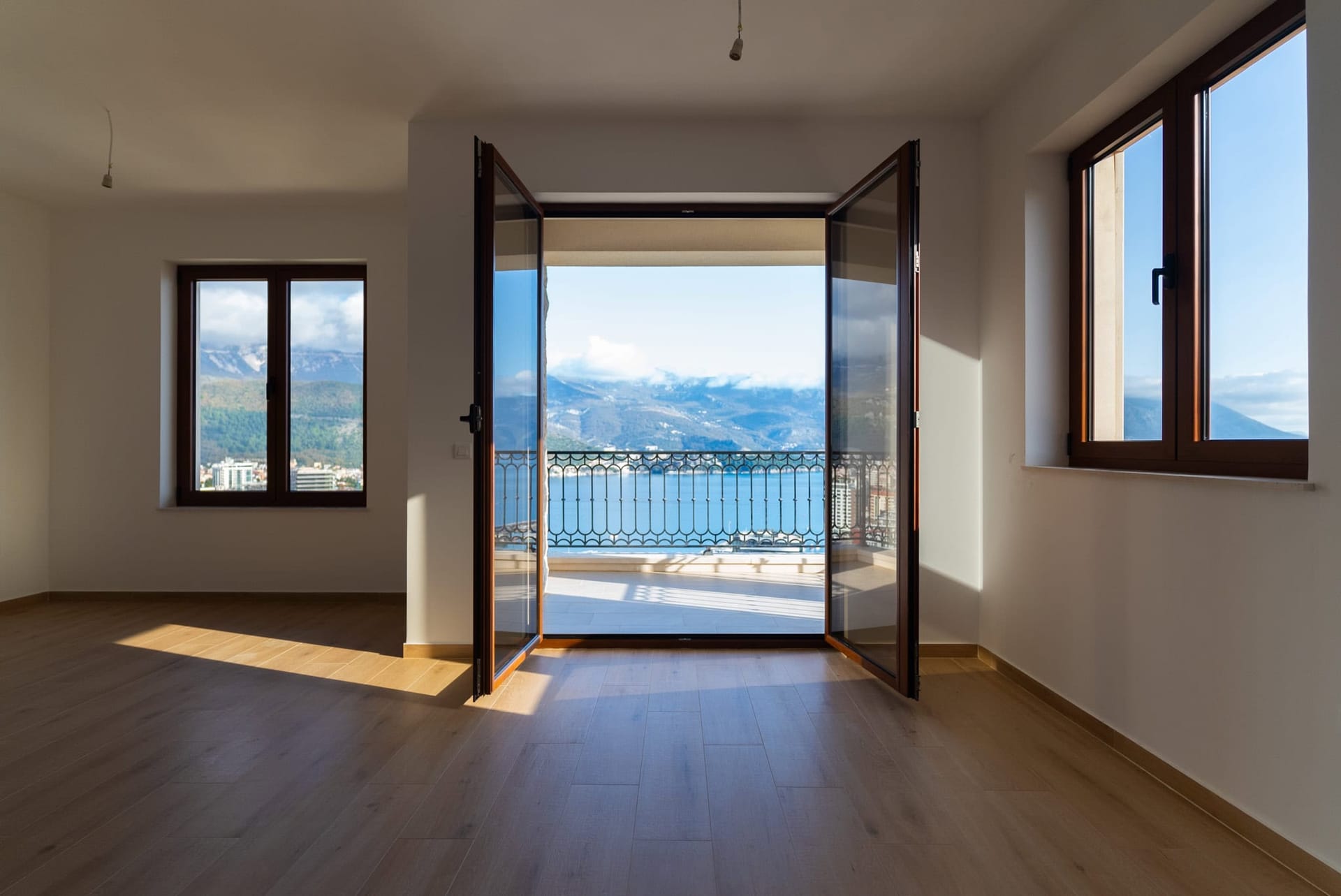 Svetao dnevni boravak sa parketom i izlazom na balkon s panoramskim pogledom na more i planine u Budvi, Crna Gora.