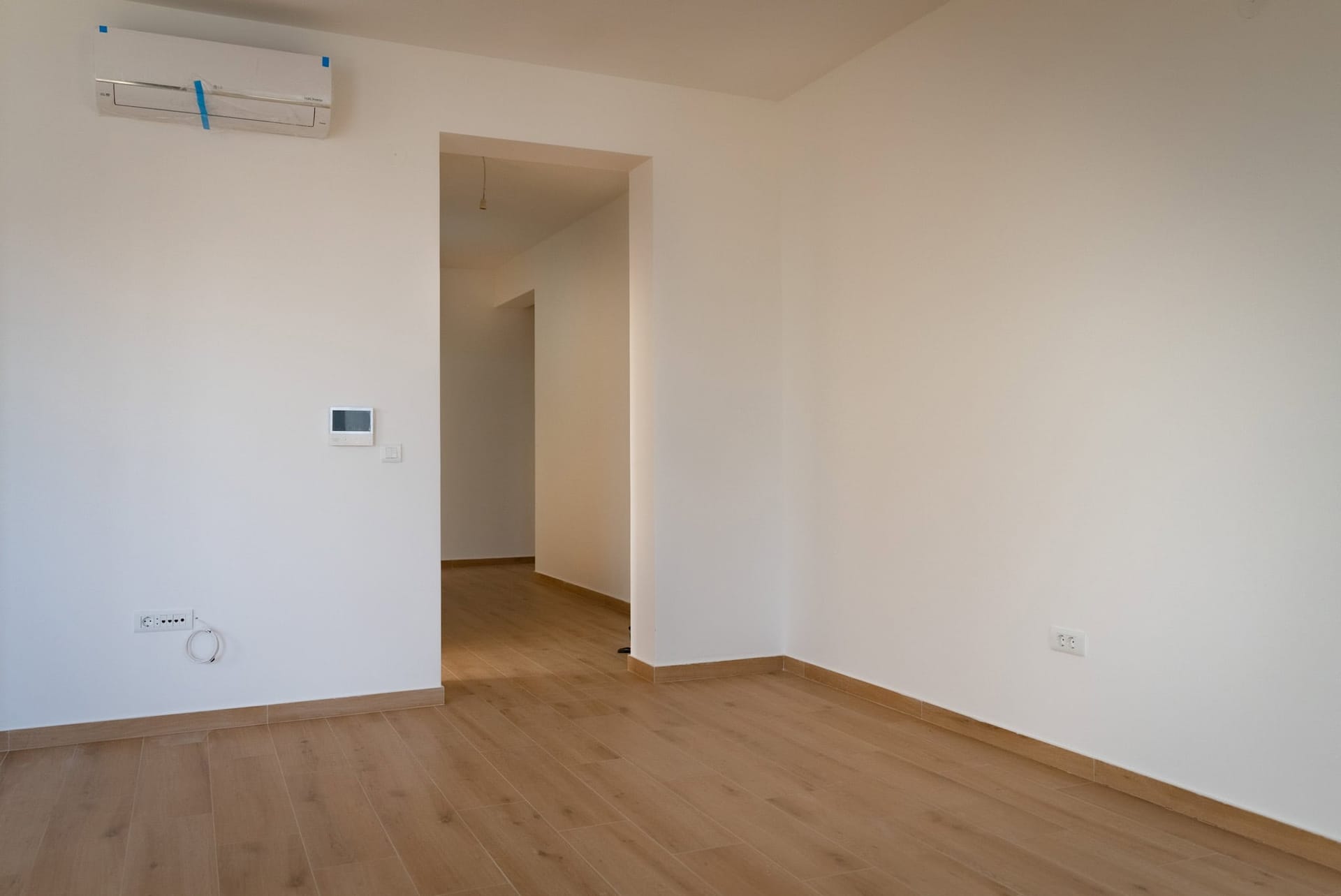 Svetao dnevni boravak u novom stanu u Budvi, Crna Gora: beli zidovi, laminat u imitaciji drveta i ugrađen klima-uređaj.