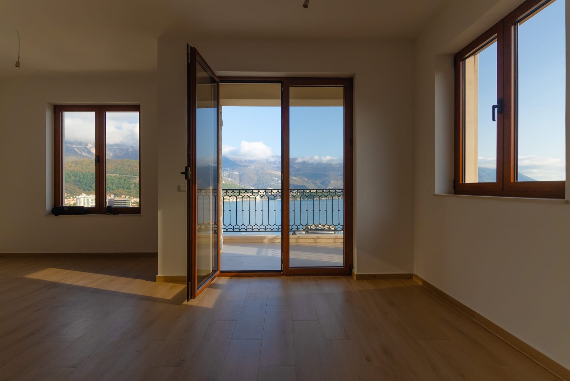 Svetla dnevna soba u Budvi, Crna Gora, sa izlazom na balkon, panoramskim pogledom na more i planine, drveni pod.